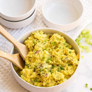 Curried Potato Salad in a bowl with two wooden spoons.