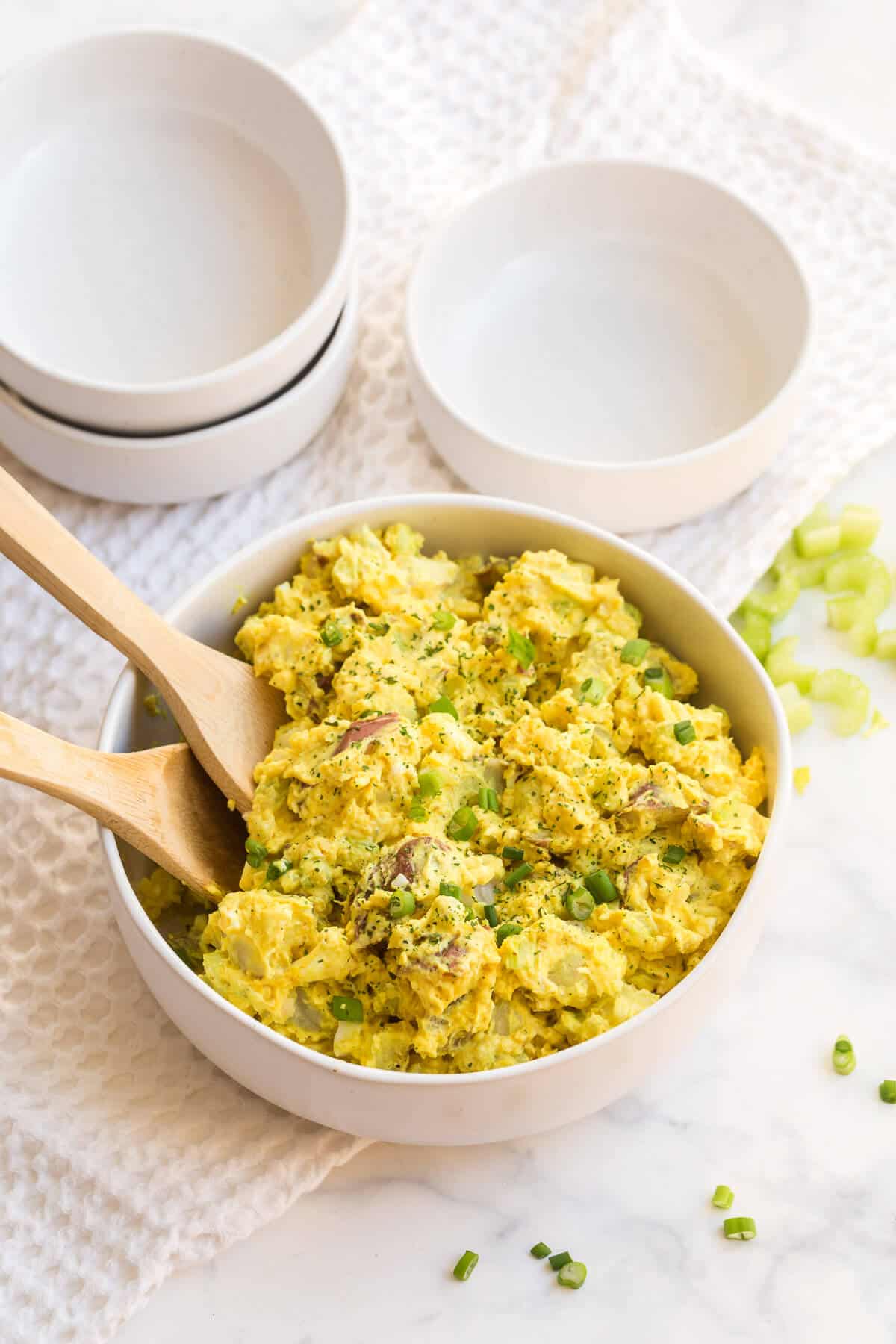 Curried Potato Salad in a bowl with two wooden spoons.