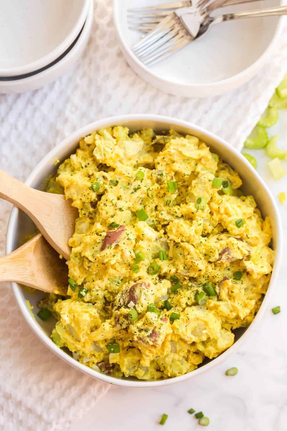 Curried Potato Salad in a bowl with two wooden spoons.