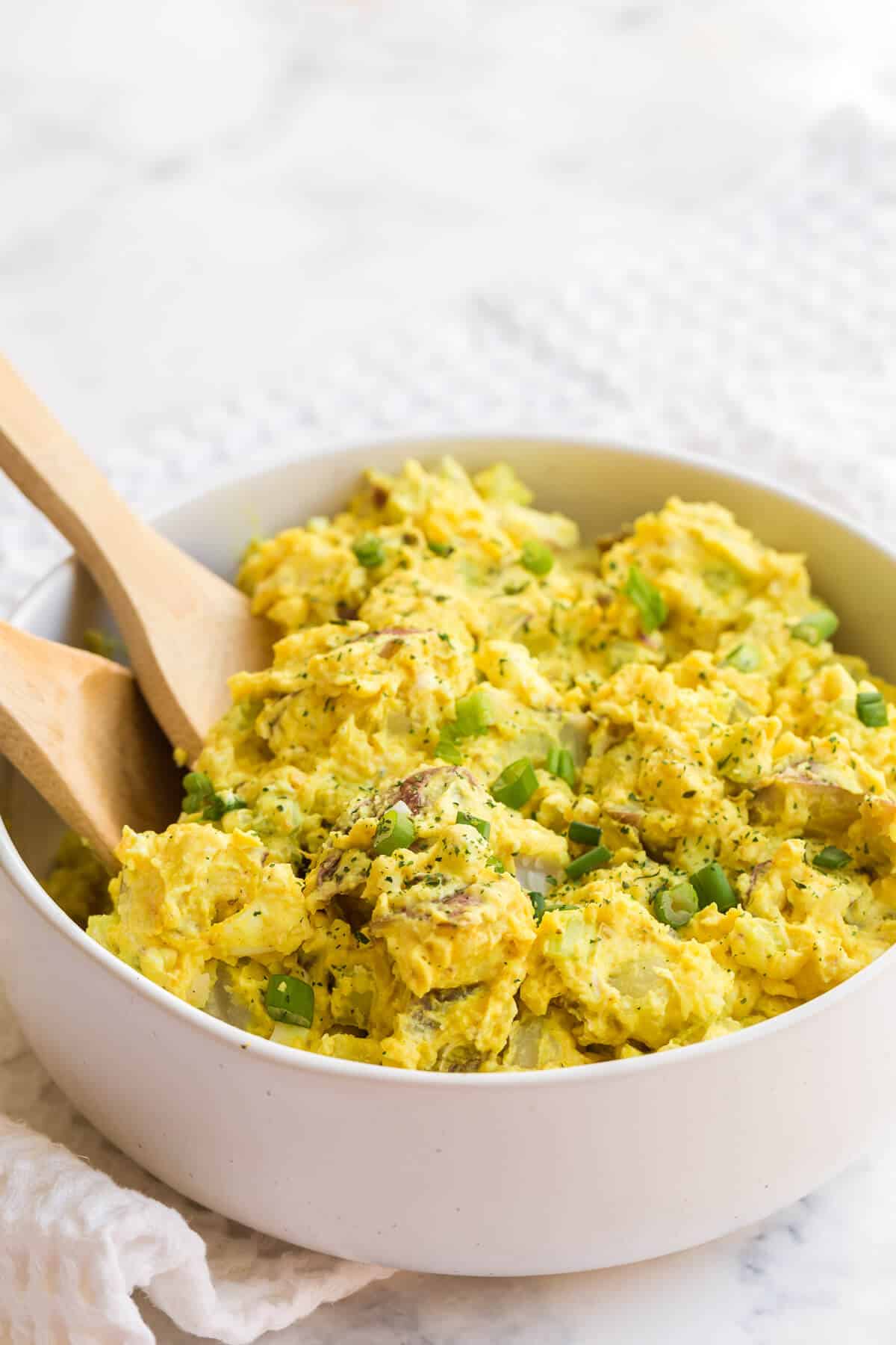 curried potato salad in a bowl with two wooden spoons.