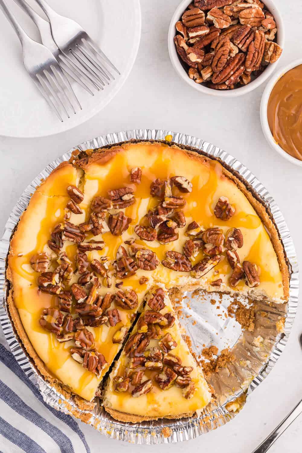A whole caramel pecan cheesecake with a slice cut