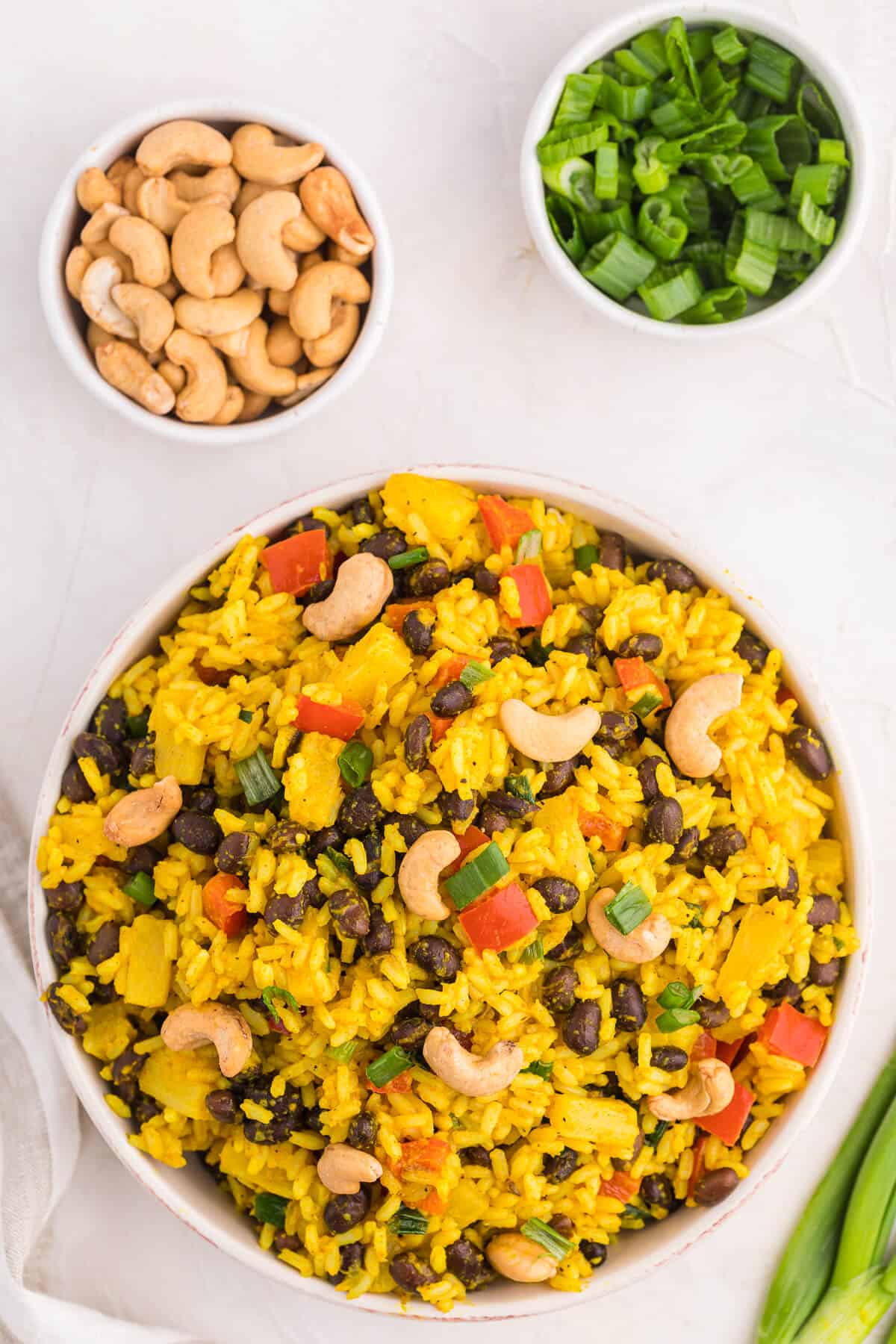 Jamaican curried rice in a bowl with cashews and green onions on the side.