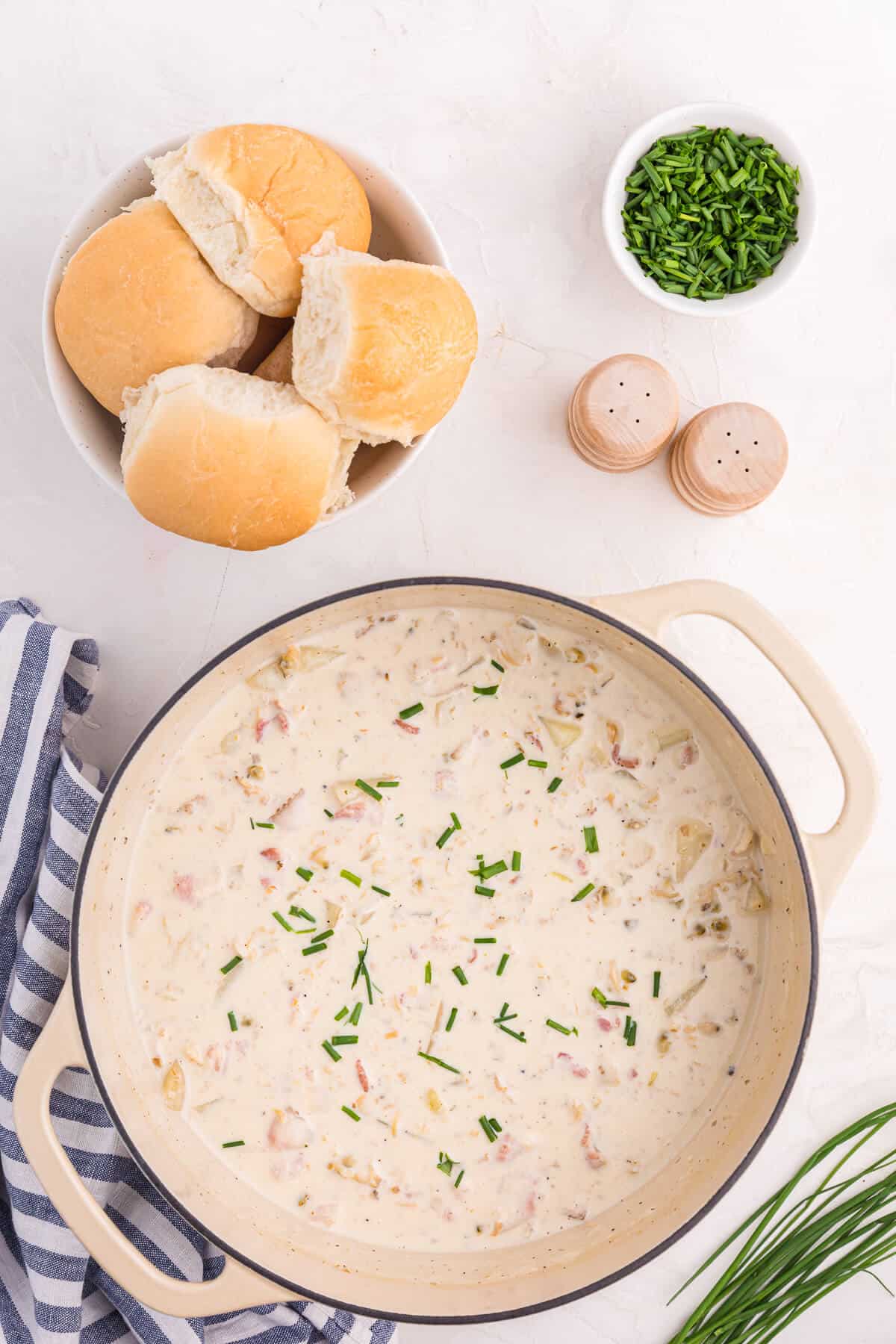 A dutch oven of New England Clam Chowder with rolls and chives.
