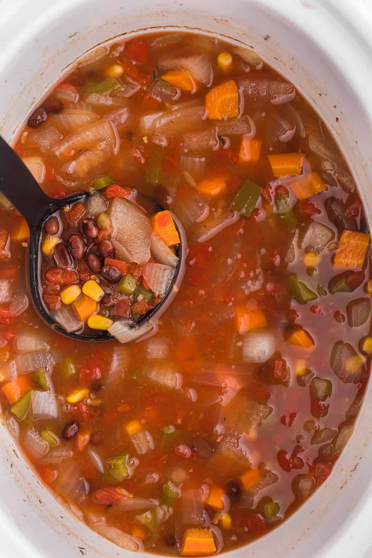 Black bean vegetable soup in the slow cooker with a ladle.