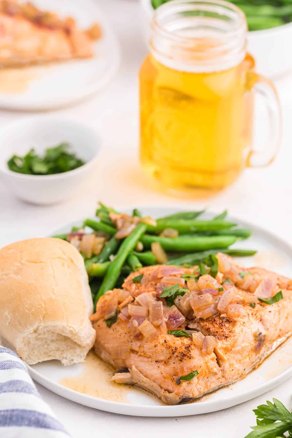 Drunken salmon with a roll and green beans on a plate.