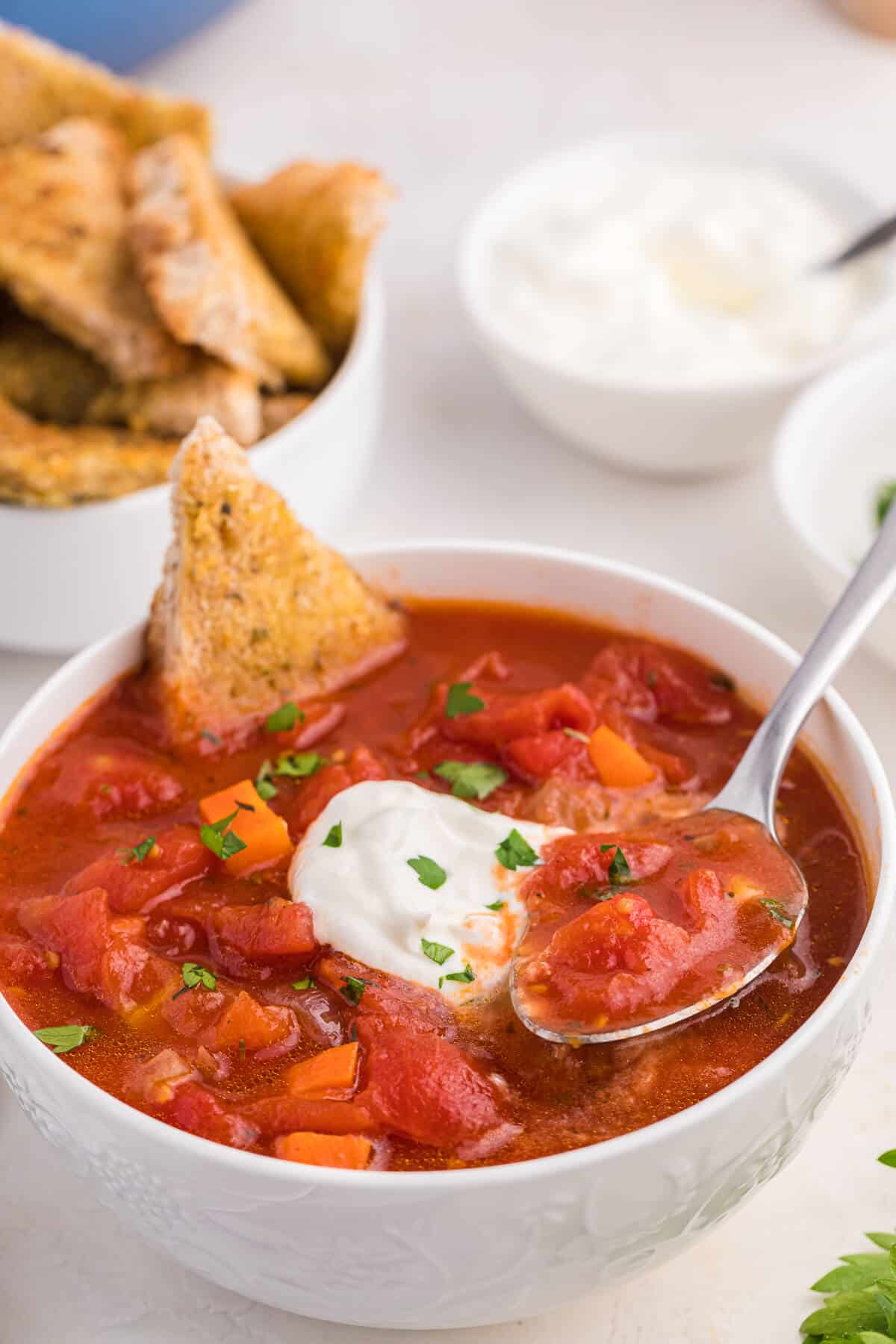 Italian herb soup in a bowl with garlic toast and a spoon.