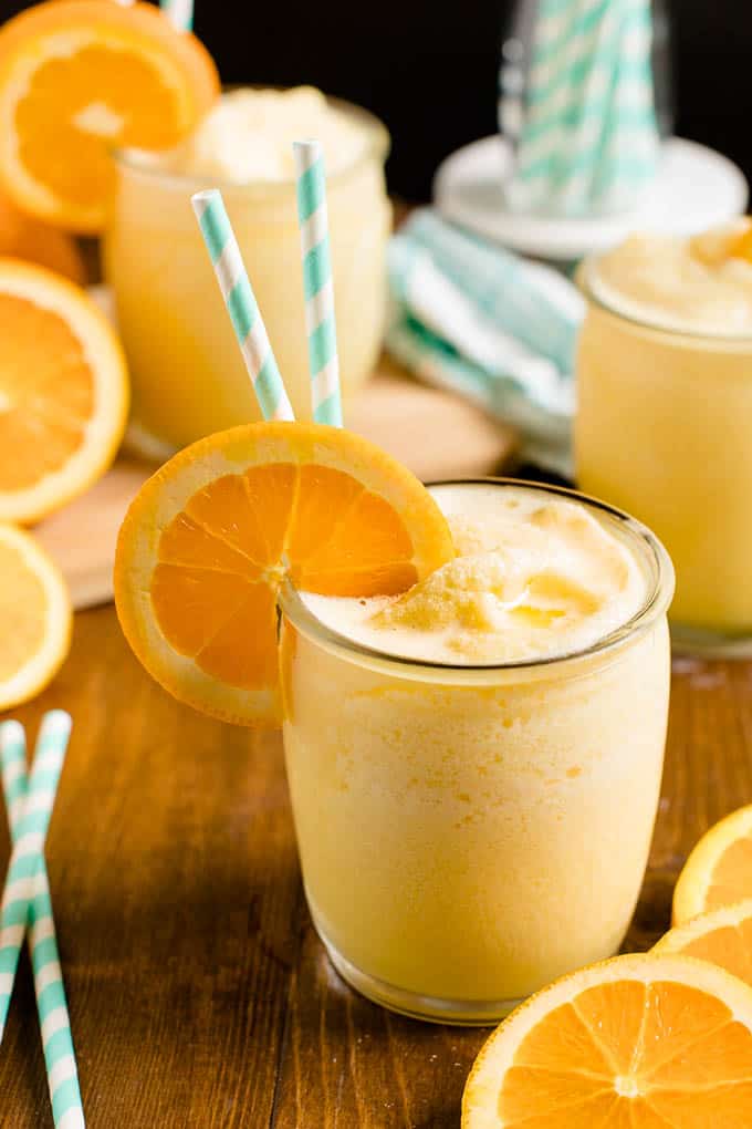 Orange julius in a glass with two striped straws and an orange slice for garnish.