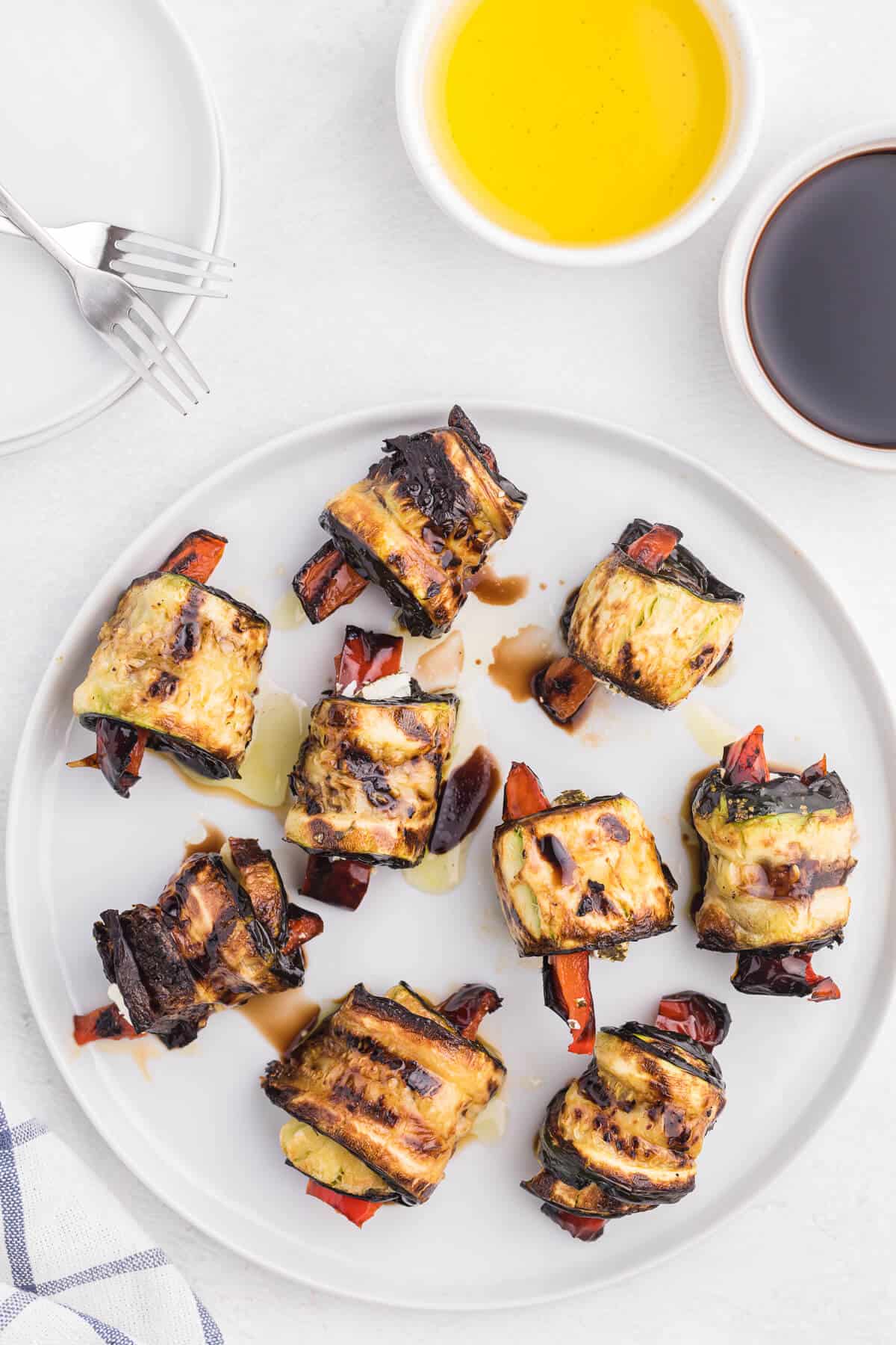 Grilled Zucchini Roll-Ups - A simple, but savory summer appetizer. This easy recipe wraps grilled zucchini strips around herbed goat cheese and grilled red peppers with a finish of extra olive oil and balsamic vinegar. Mmm!