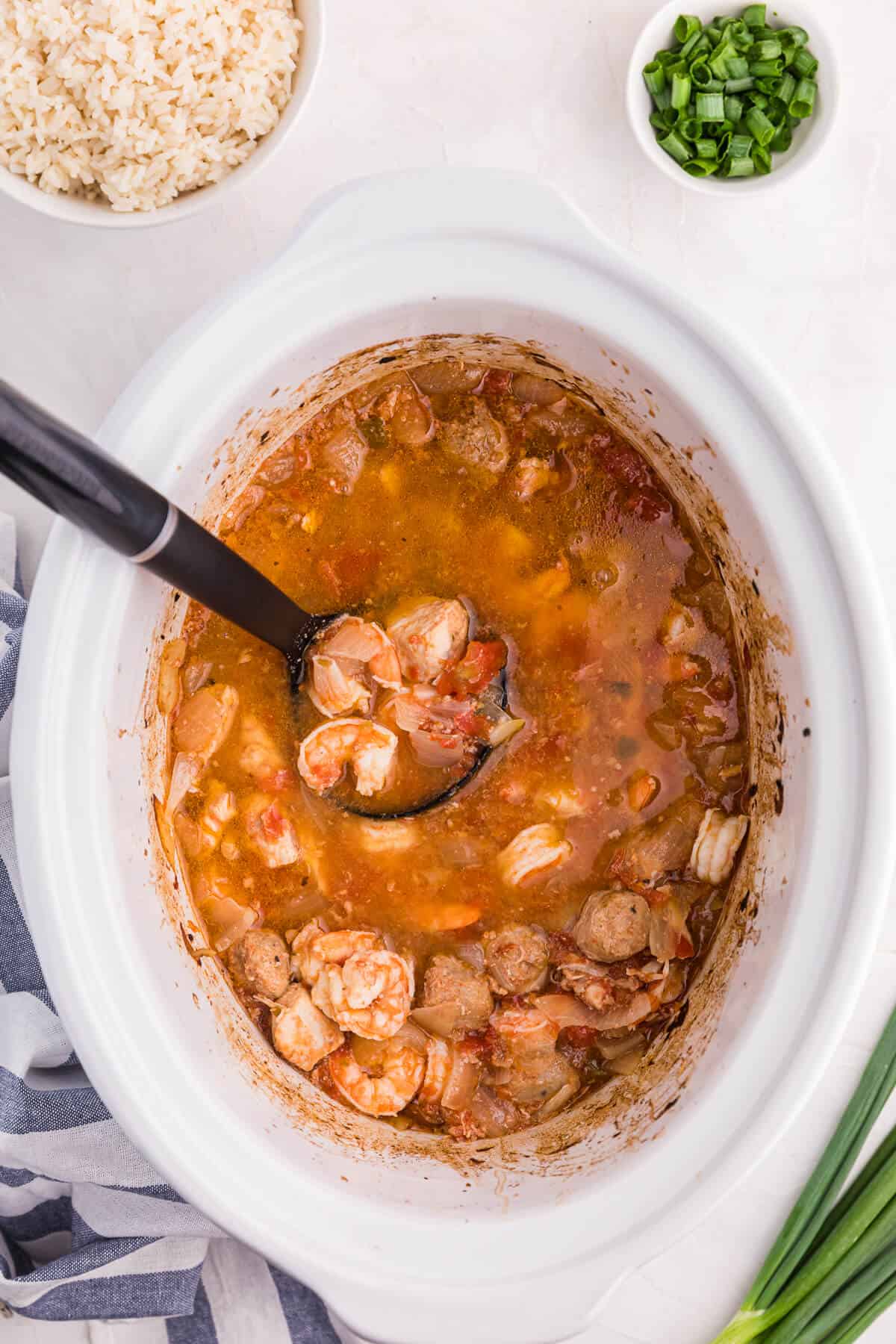 Sausage jambalaya in a white crockpot with a ladle in it.