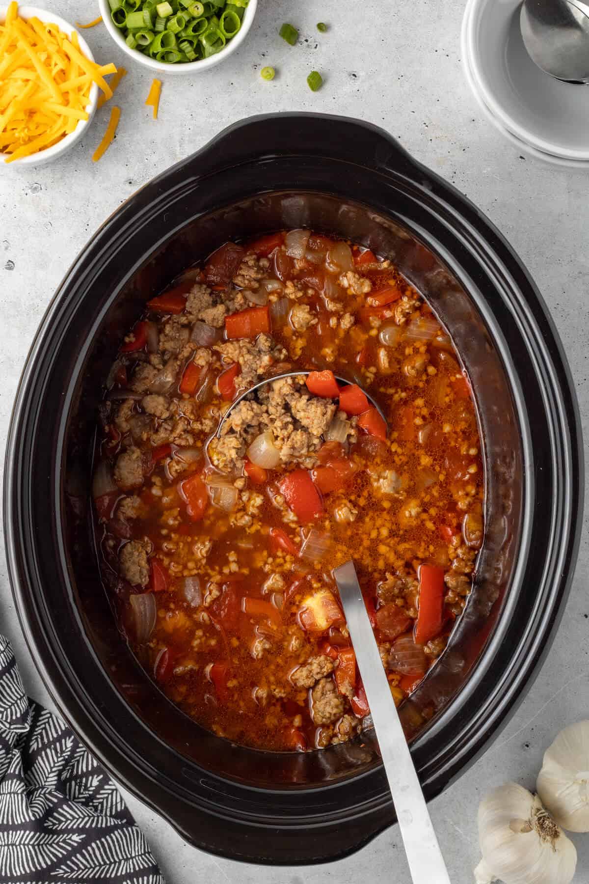 A crockpot of spicy sausage soup with a ladle.