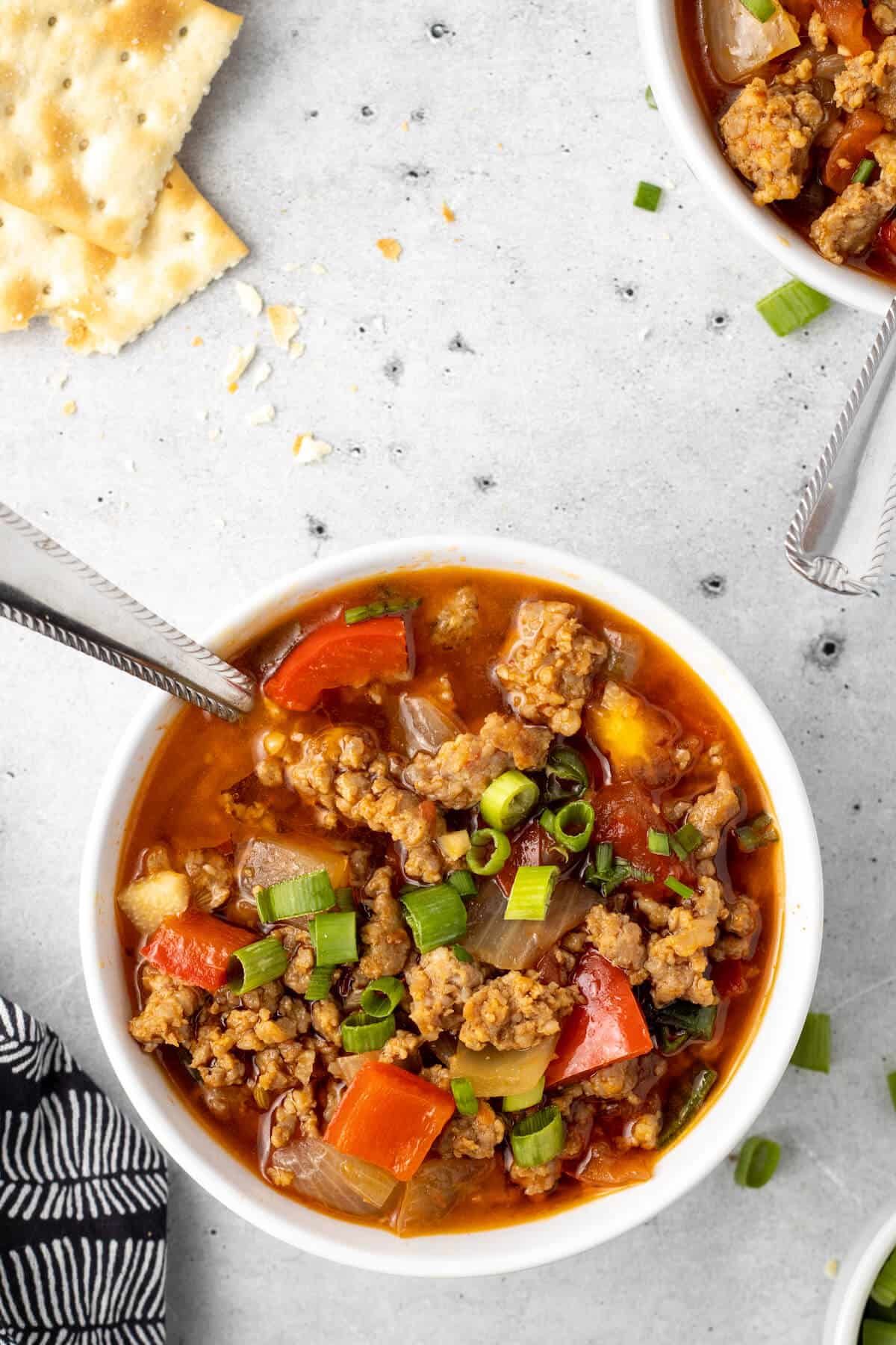 A bowl of spicy sausage soup with a spoon.