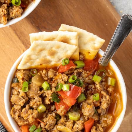 A bowl of spicy sausage soup with crackers and spoon.