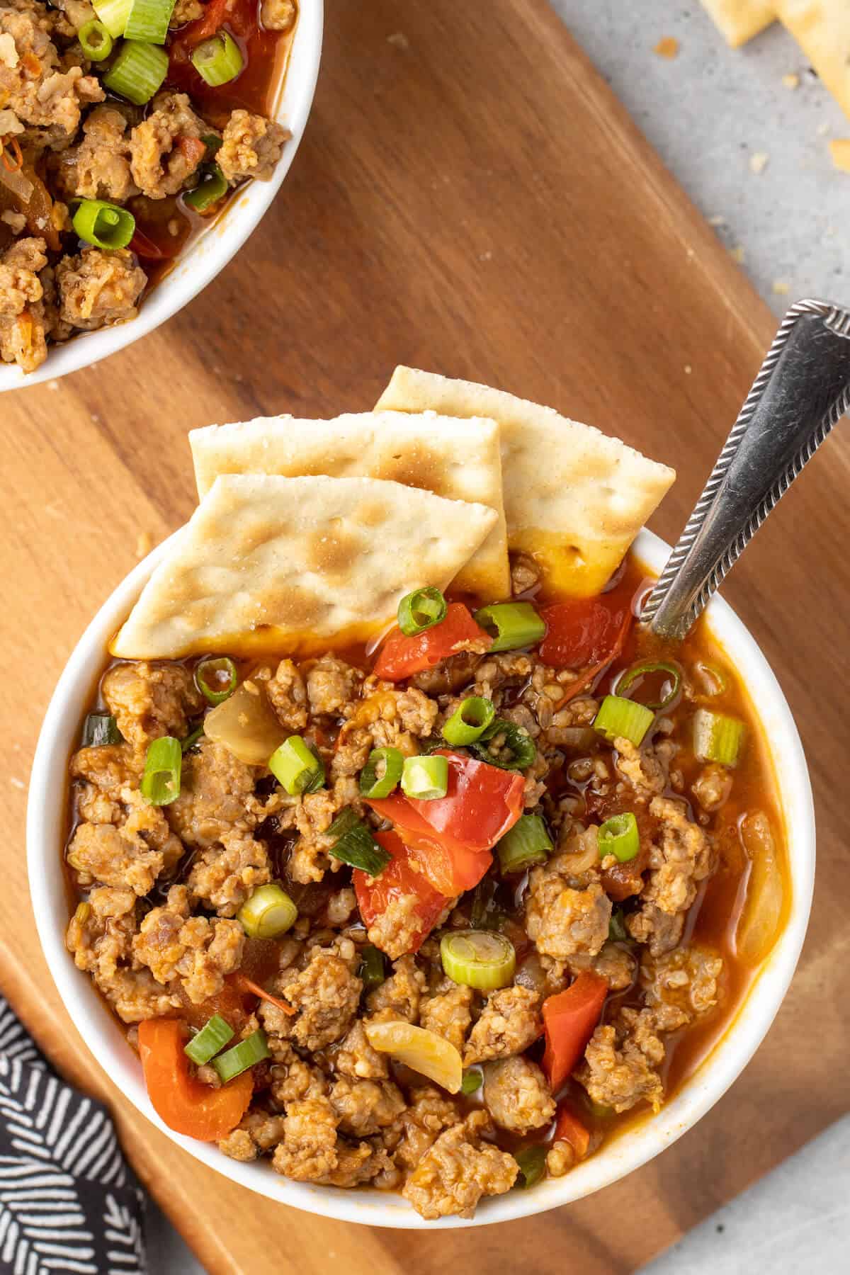 A bowl of spicy sausage soup with crackers and spoon.