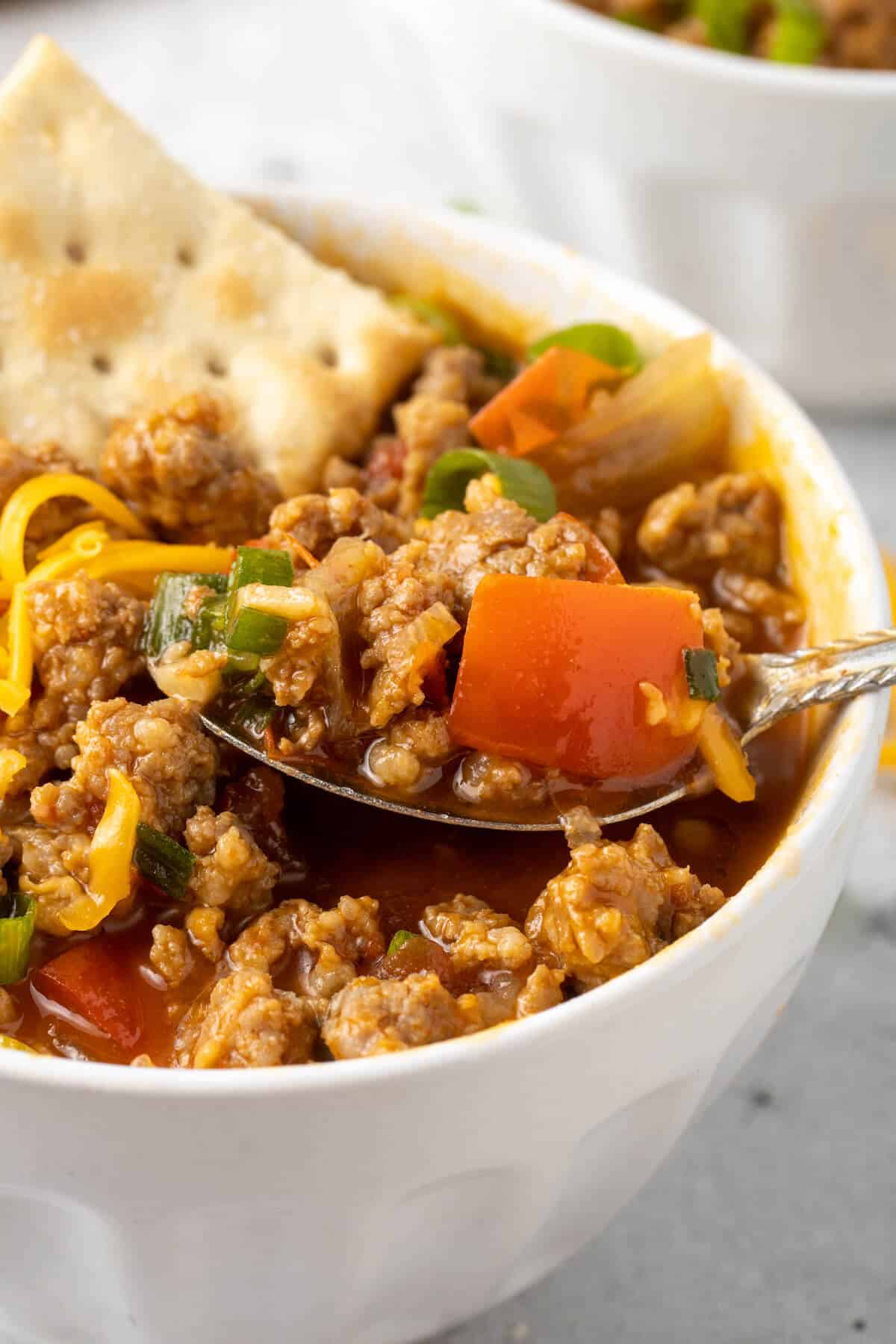 Spicy sausage soup in a bowl with a spoon.