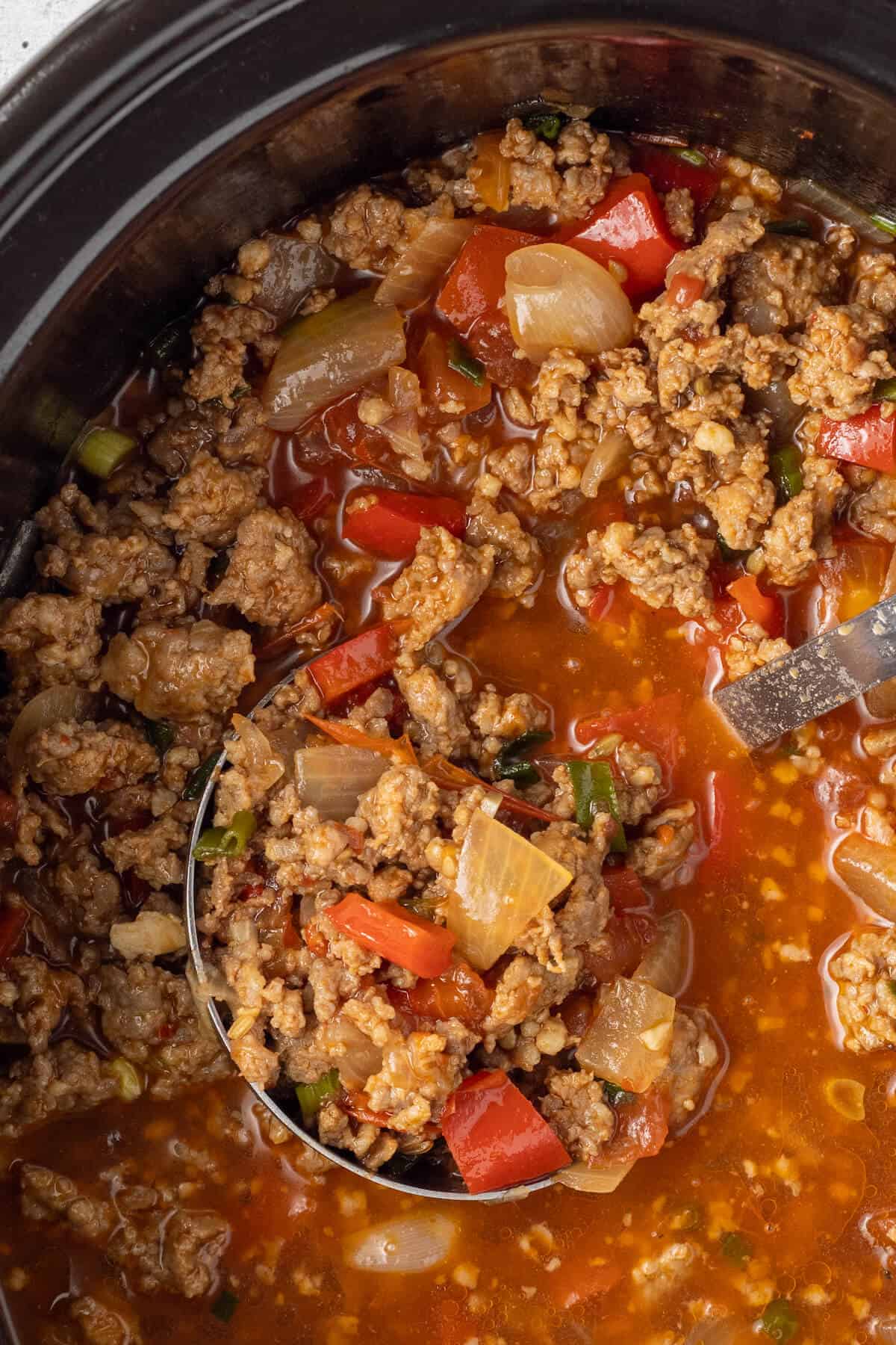 A ladle in a crockpot of spicy sausage soup.