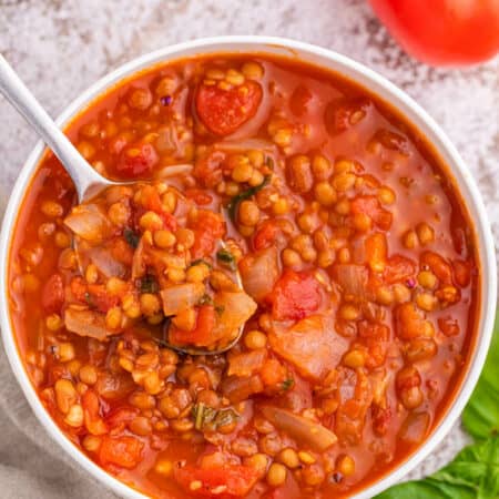 A bowl of tomato lentil soup with a spoon in it.