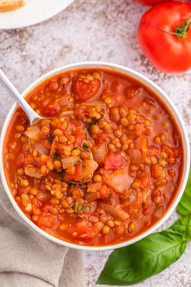 A bowl of tomato lentil soup with a spoon in it.