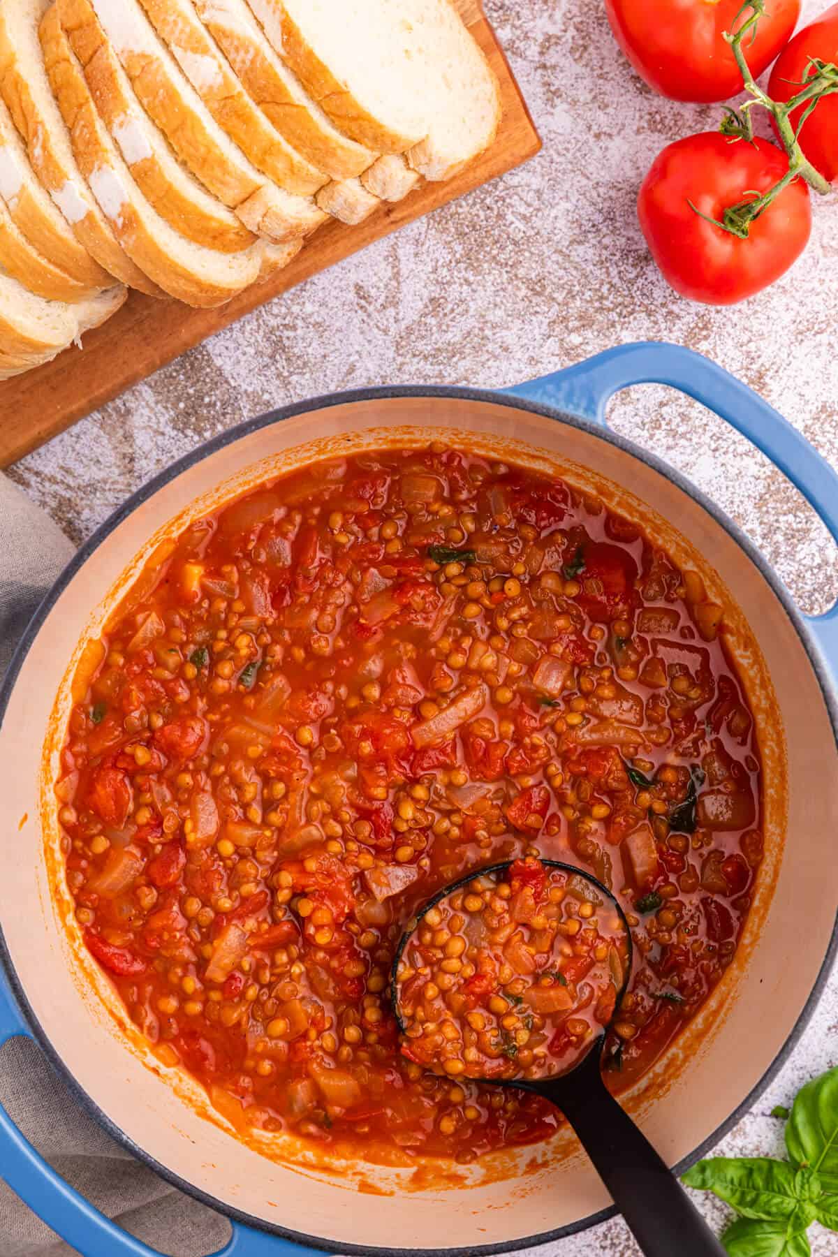 A pot of tomato lentil soup with a ladle.