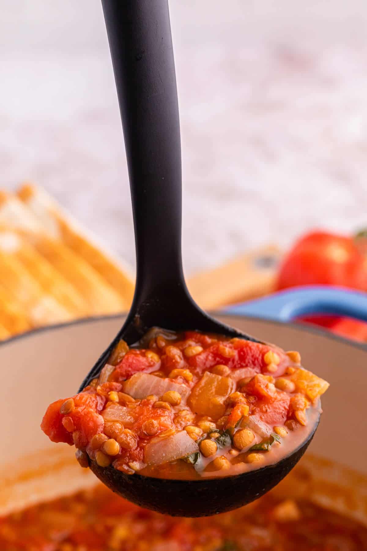 A black ladle with tomato lentil soup.