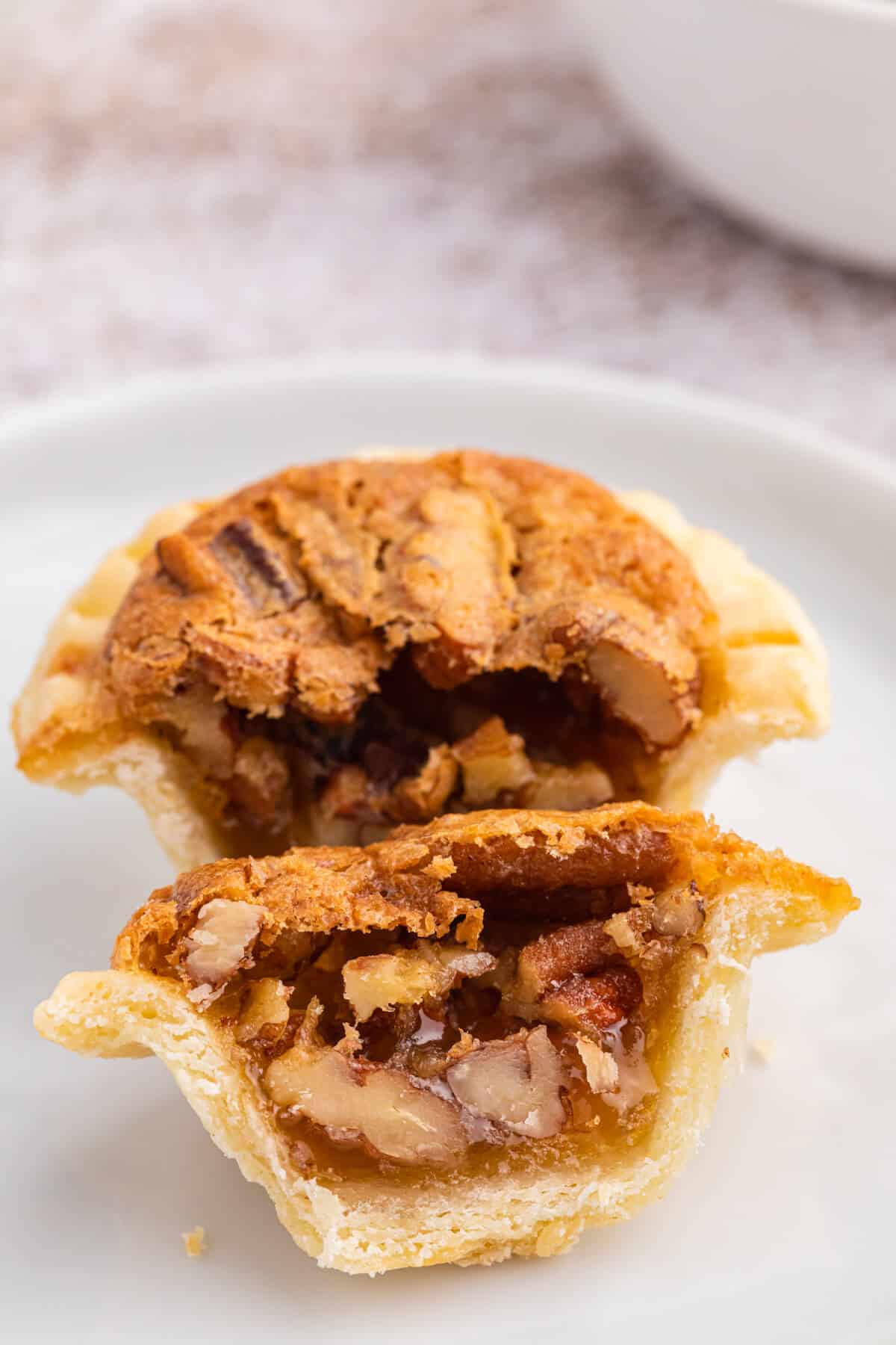 A pecan butter tart cut in half on a plate.