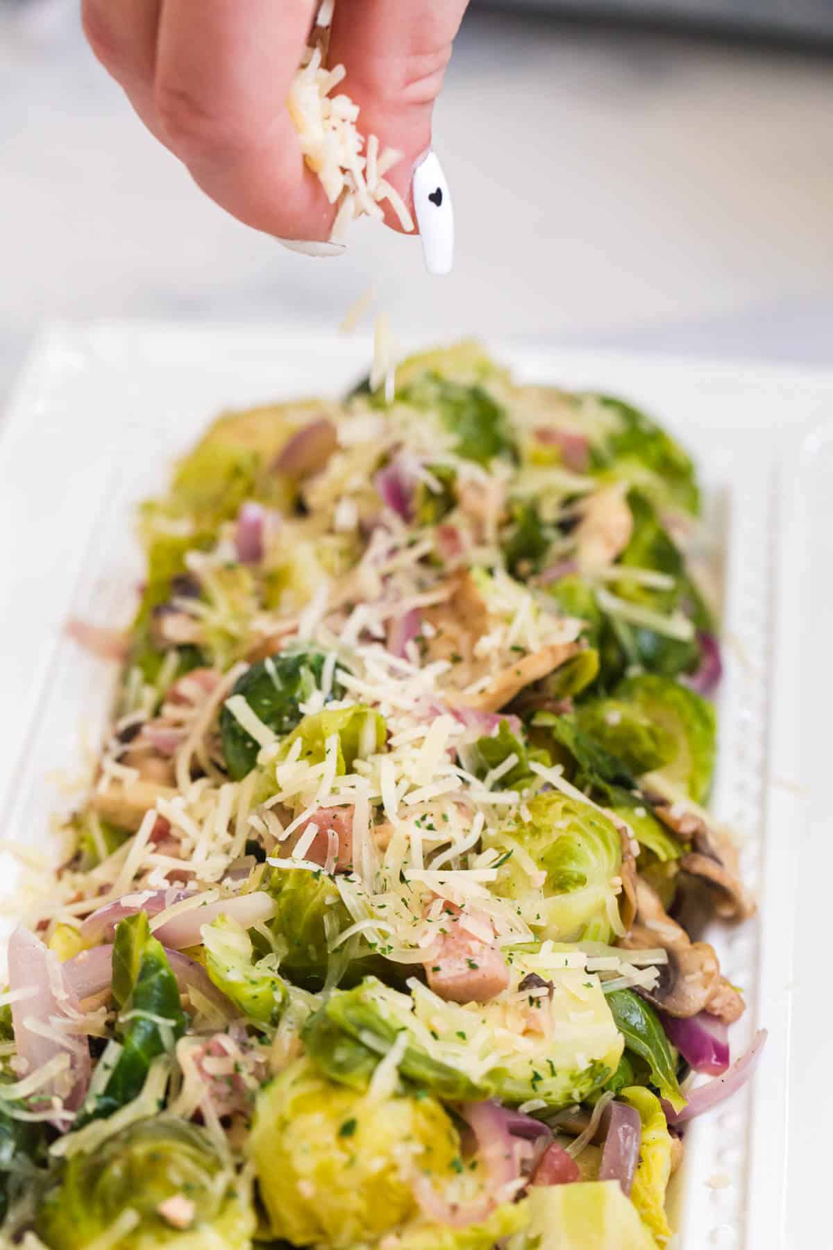 A hand sprinkling parmesan cheese on brussel sprouts.