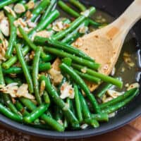 Chili buttered green beans in a skillet with a wooden spoon.