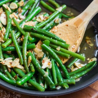 Chili buttered green beans in a skillet with a wooden spoon.