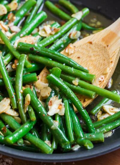 Chili buttered green beans in a skillet with a wooden spoon.