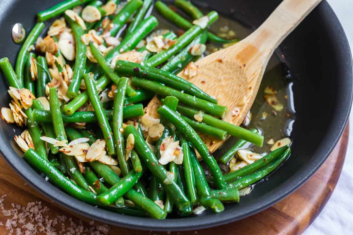 Chili buttered green beans in a skillet with a wooden spoon.