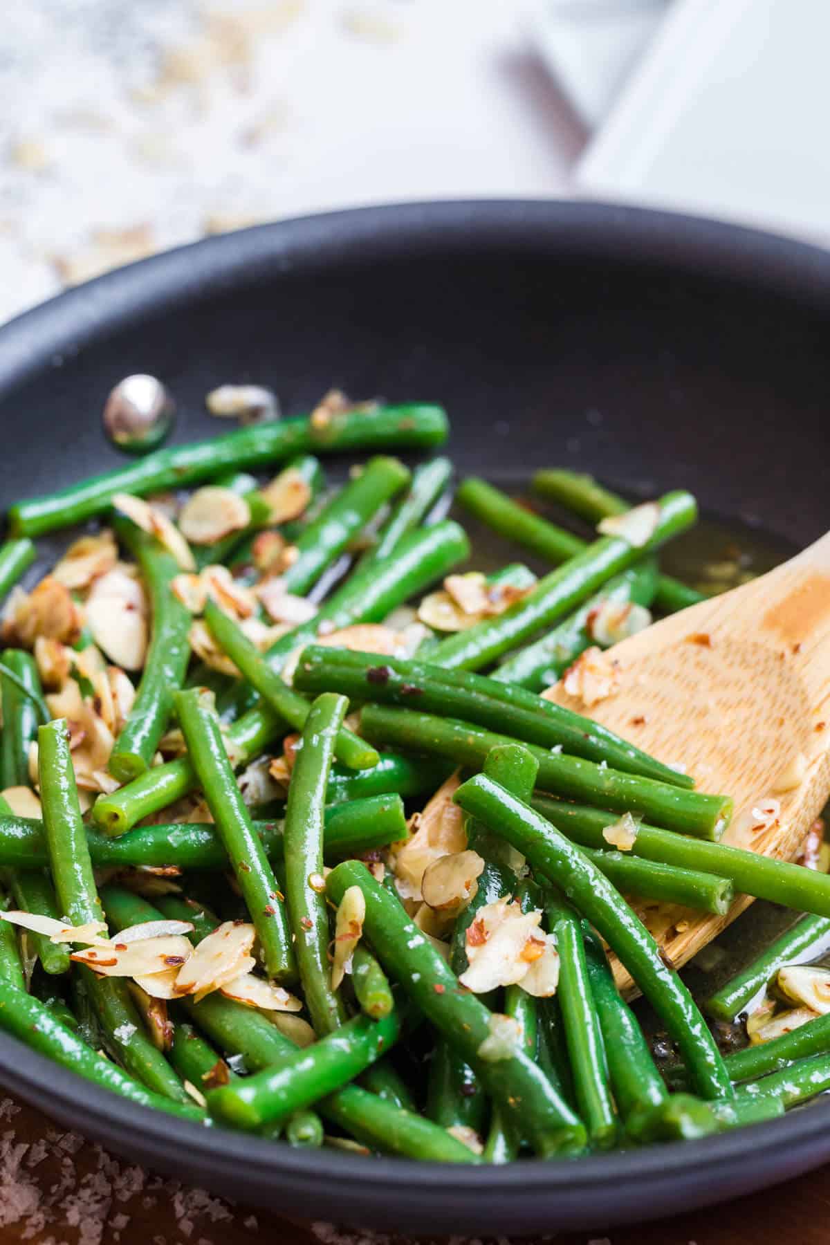 Chili Buttered green beans in a skillet with a wooden spoon.