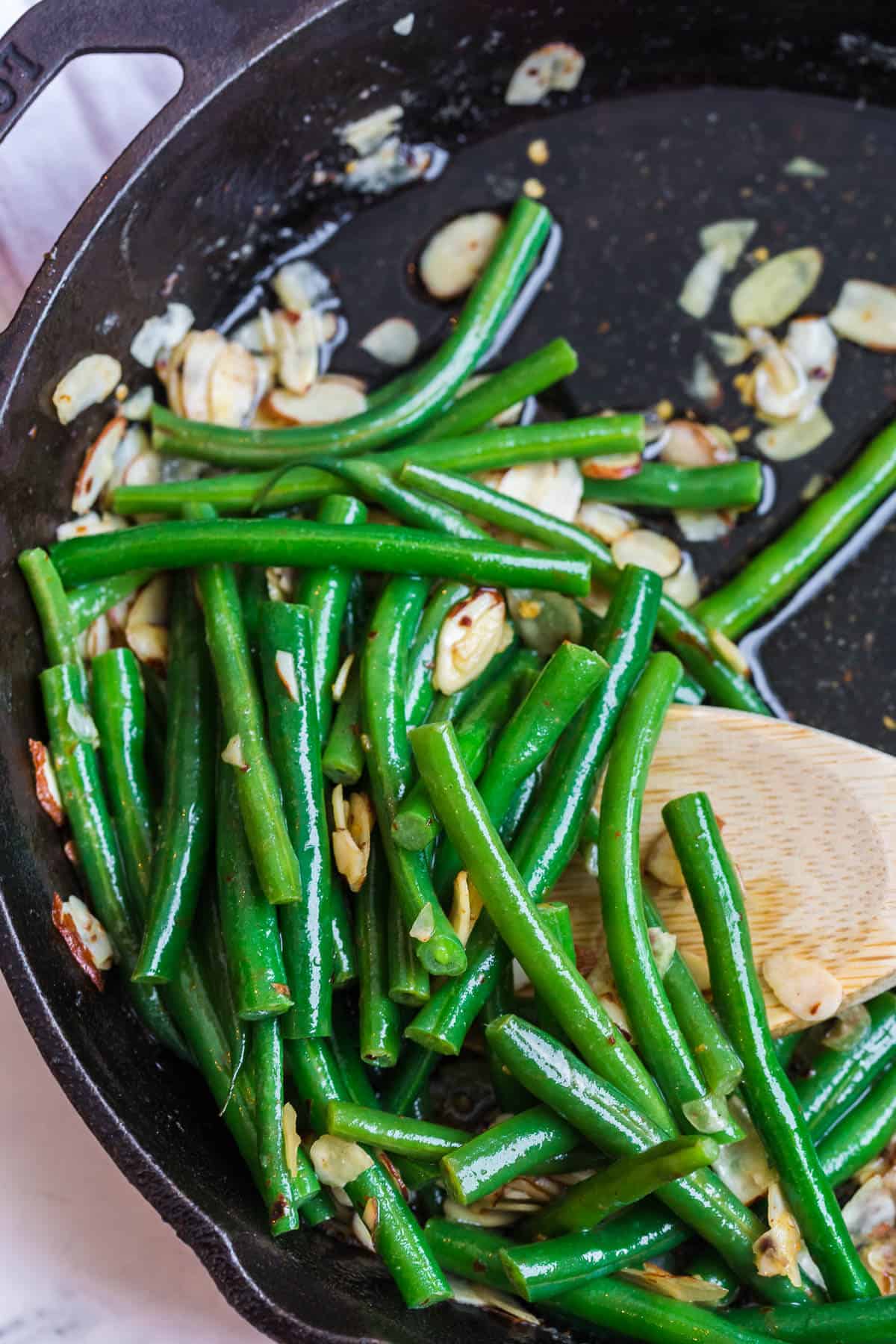 Chili buttered green beans in a skillet with a wooden spoon.