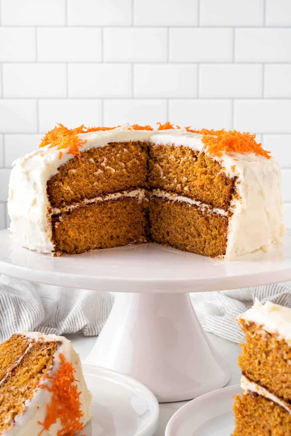 Carrot cake on a cake stand with pieces cut out of it.