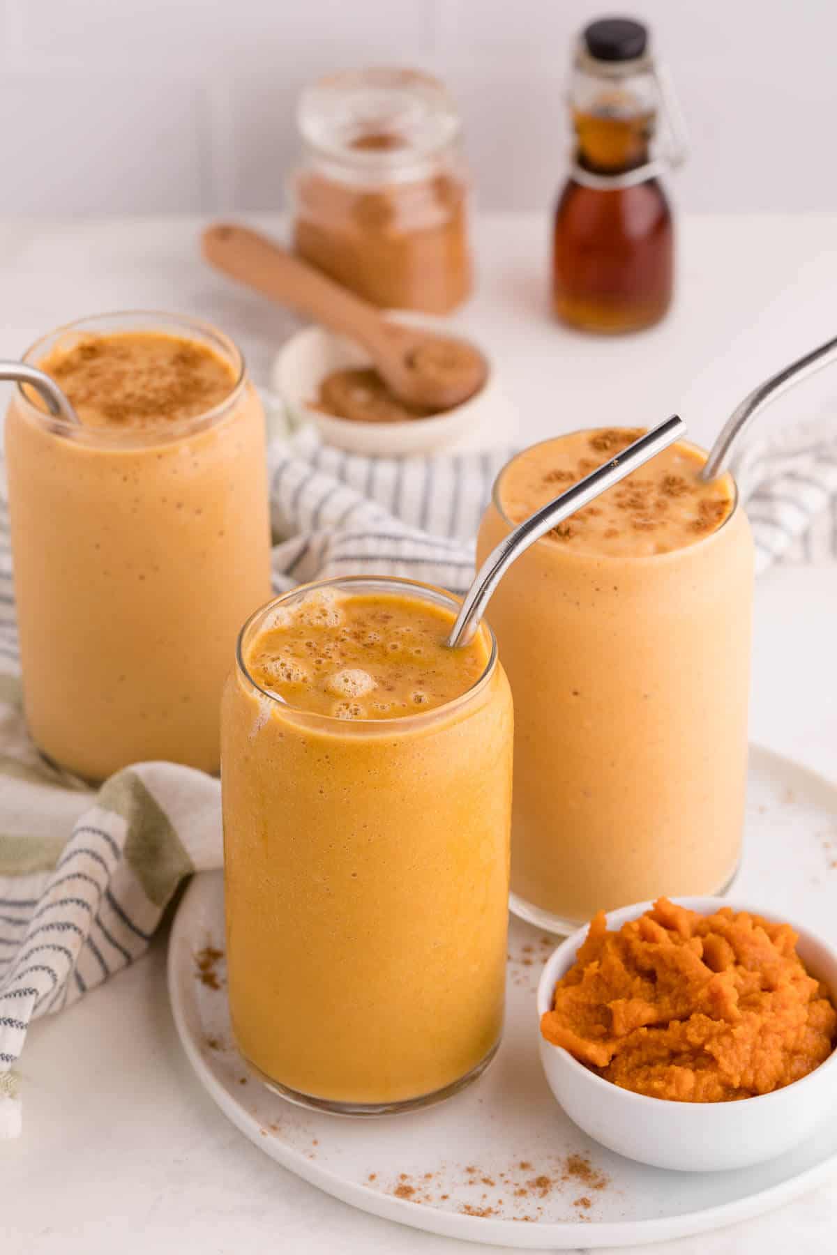 Three pumpkin pie smoothies with metal straws.