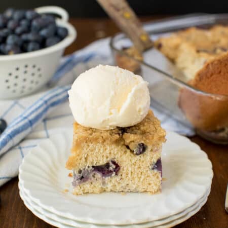 A piece of blueberry buckle on a plate topped with ice cream.