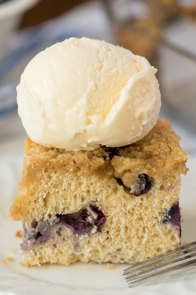 A piece of blueberry buckle with a scoop of vanilla ice cream on top.