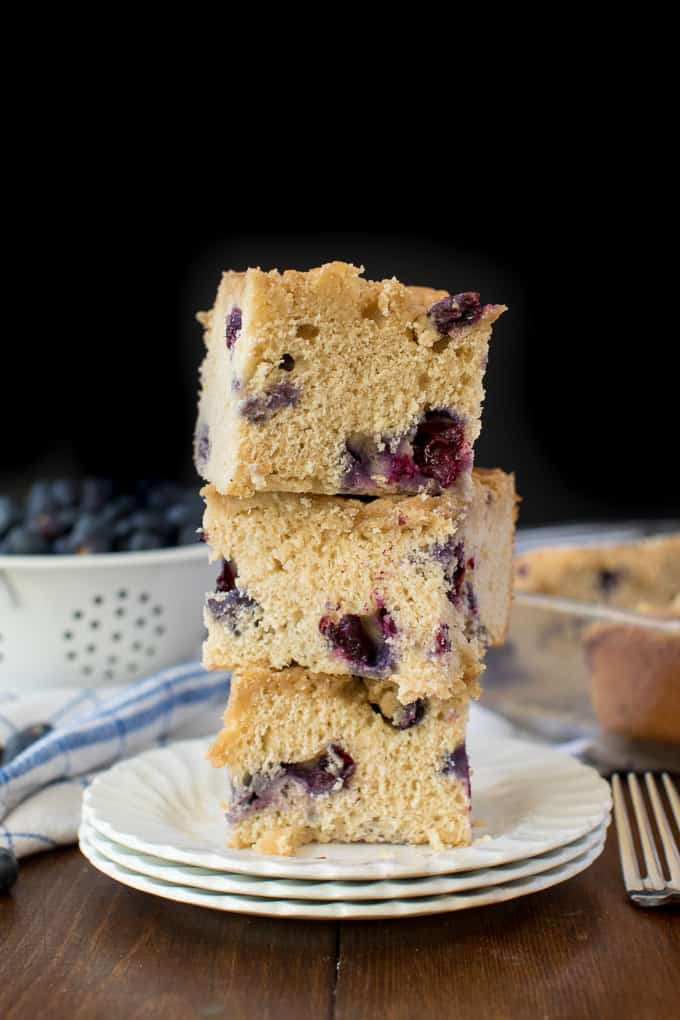 A stack of three pieces of blueberry buckle on a plate.