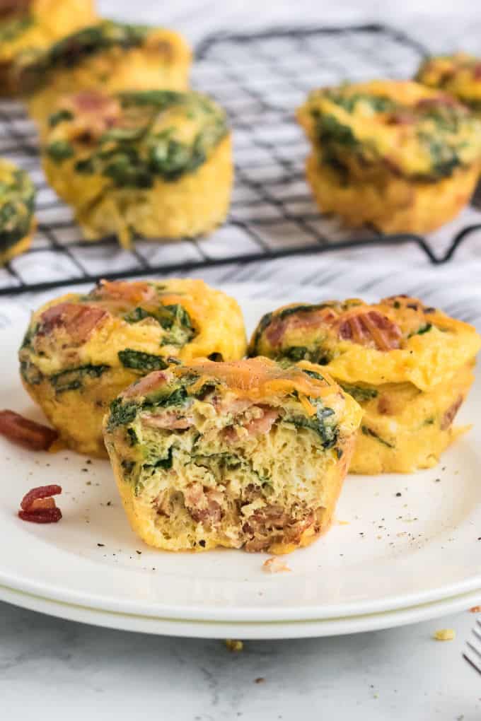 A plate of spinach and cheese egg muffins on a plate with a muffin cut in half.