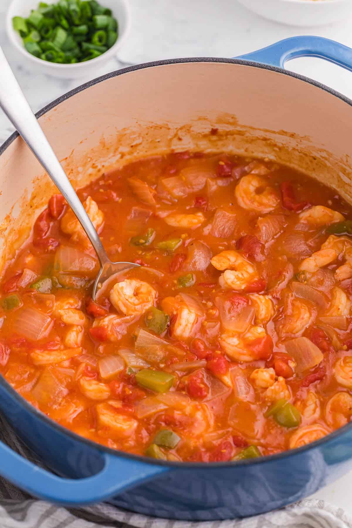 Shrimp creole in a dutch oven with a serving spoon.