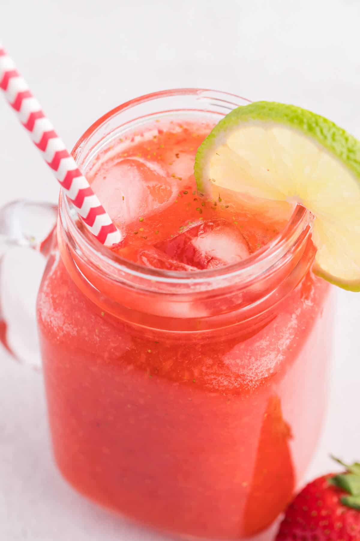 Photo of strawberry agua fresca with a straw and a lime garnish.