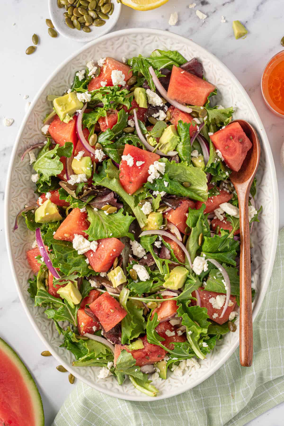 Watermelon and feta salad on a white platter with a serving spoon.