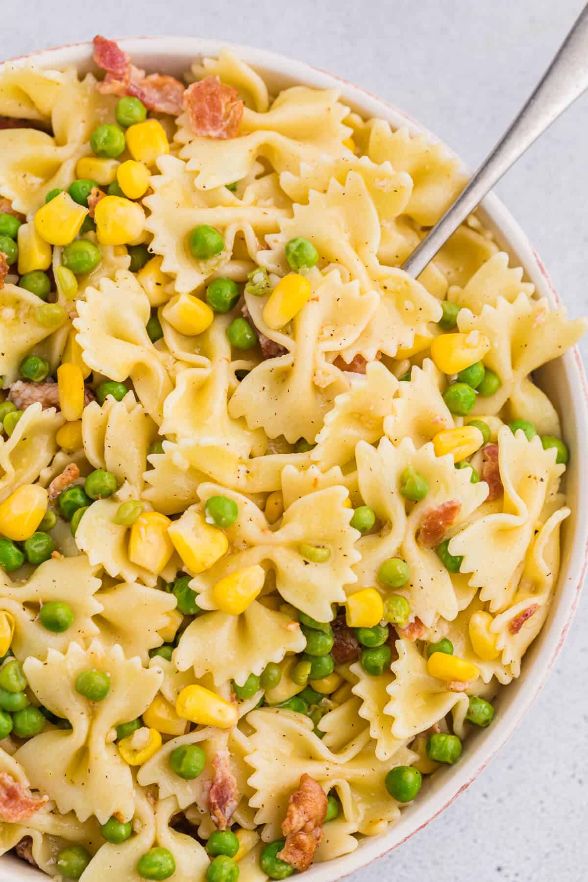 A bowl of bacon pea pasta salad with a spoon.