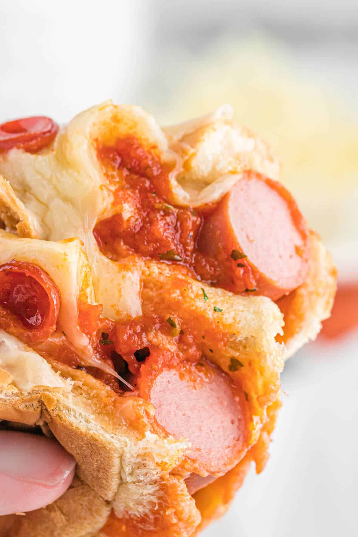 A pizza hot dog cut in half being held by a hand.
