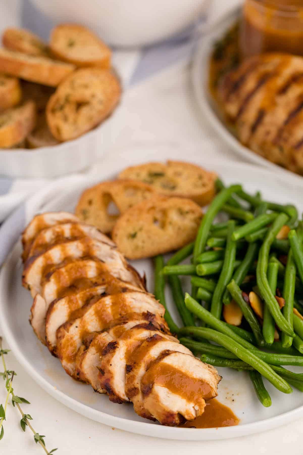 Sliced grilled herb chicken on a plate with garlic bread and green beans.