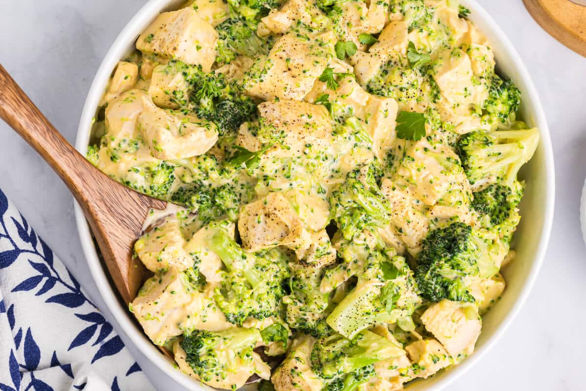 Cheesy chicken and broccoli in a bowl with a wooden spoon.