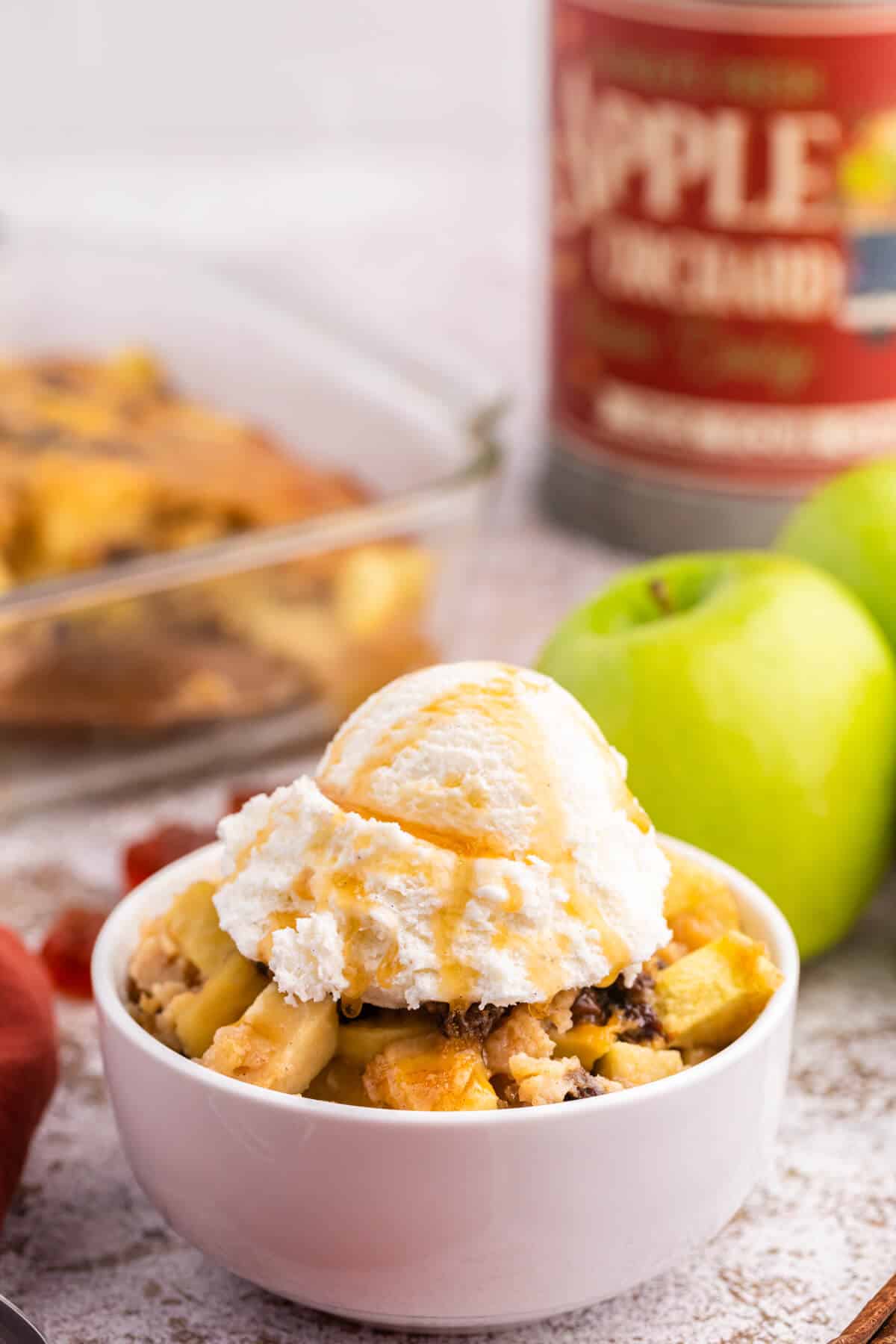 A bowl of maple apple pudding with vanilla ice cream and maple syrup on top.