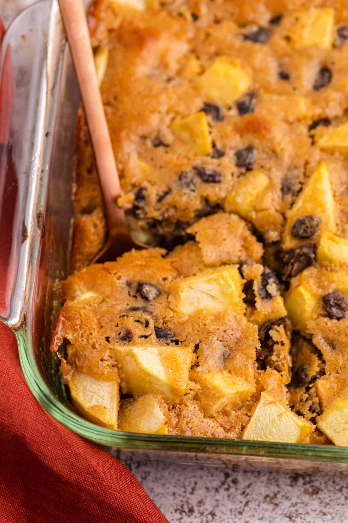 A serving spoon in a pan of maple apple pudding.