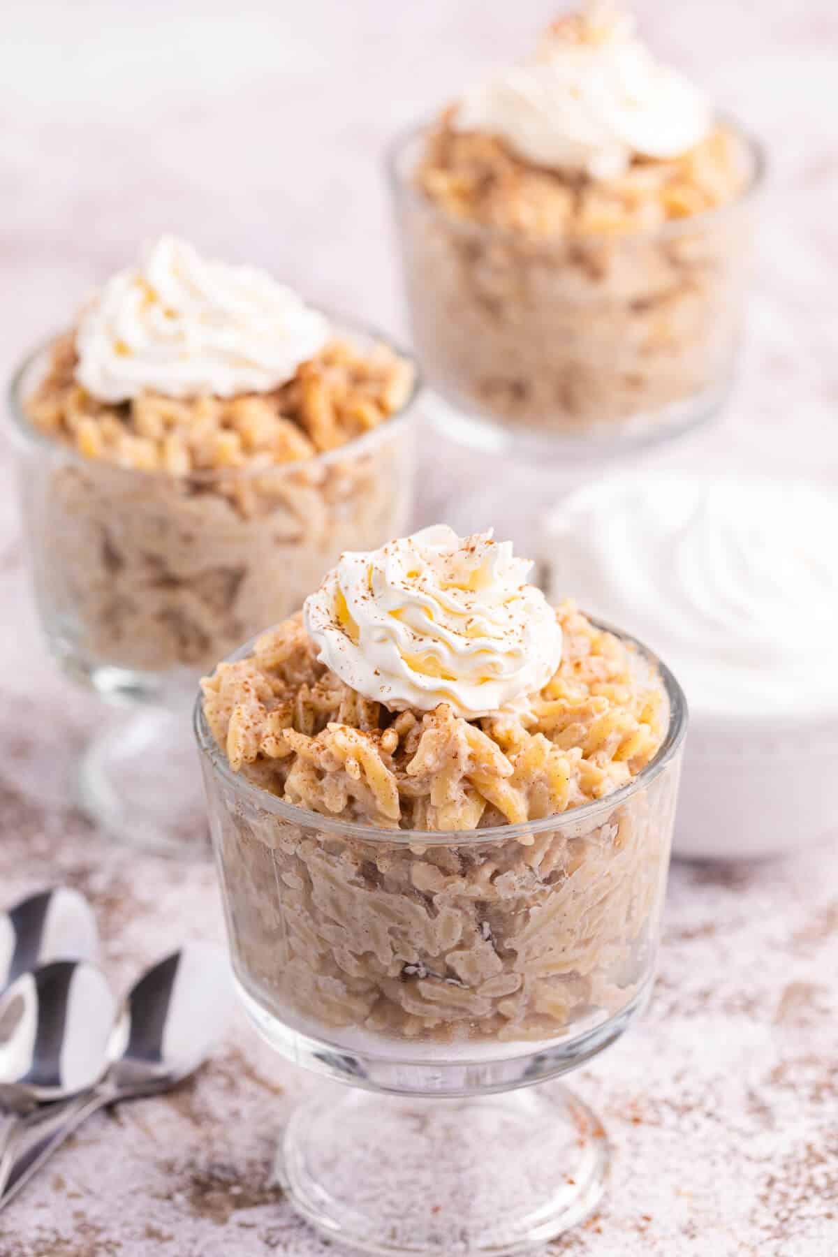 Orzo pudding topped with whipped cream in a parfait dish.
