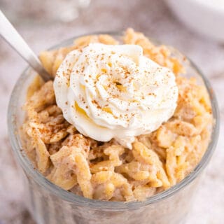 Orzo pudding topped with whipped cream in a parfait dish with a spoon.