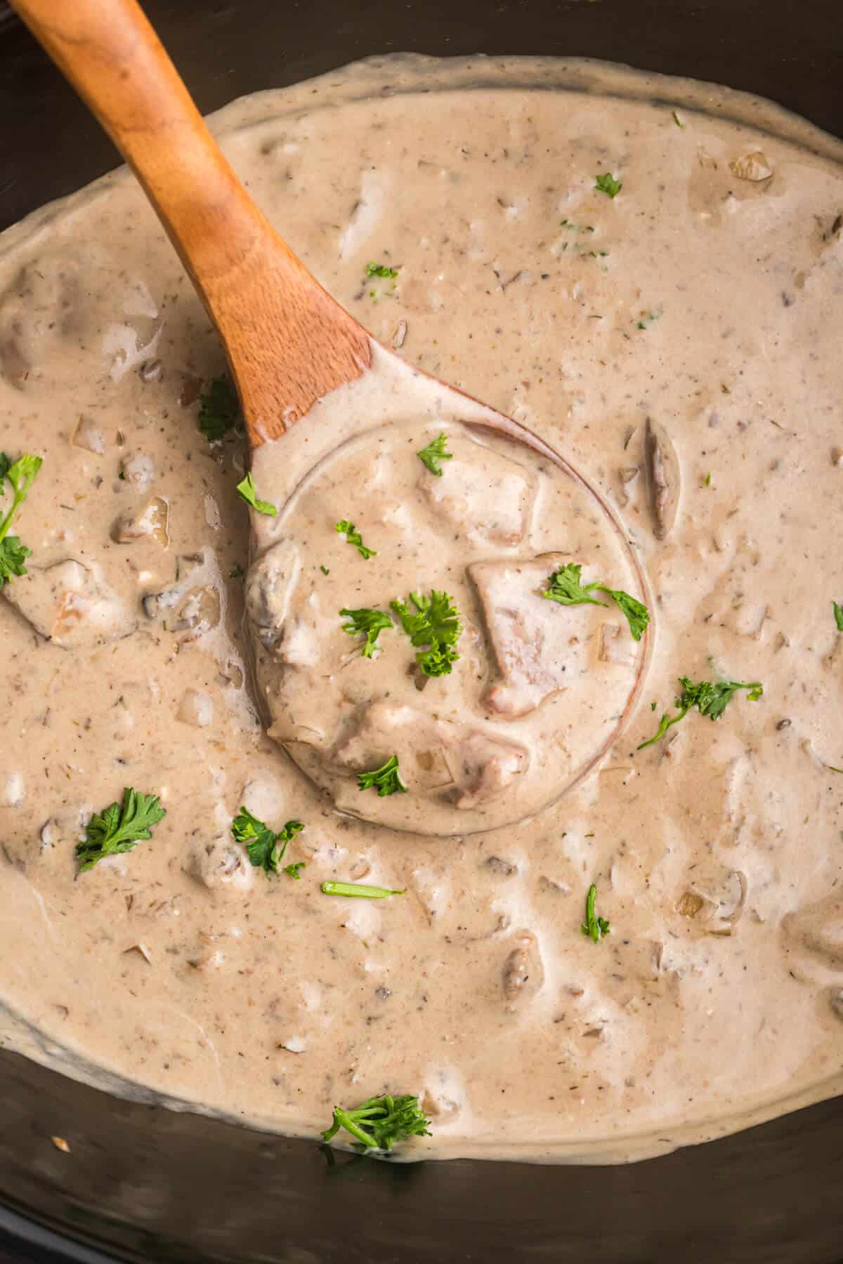 A wooden spoon in a crockpot of beef stroganoff.