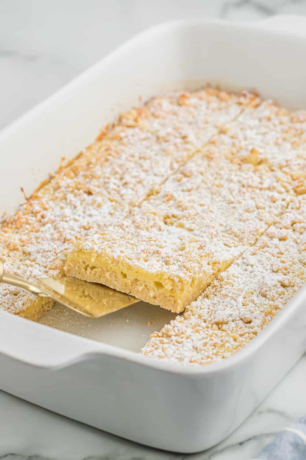 french vanilla cream bars in a casserole pan with a spatula serving a piece